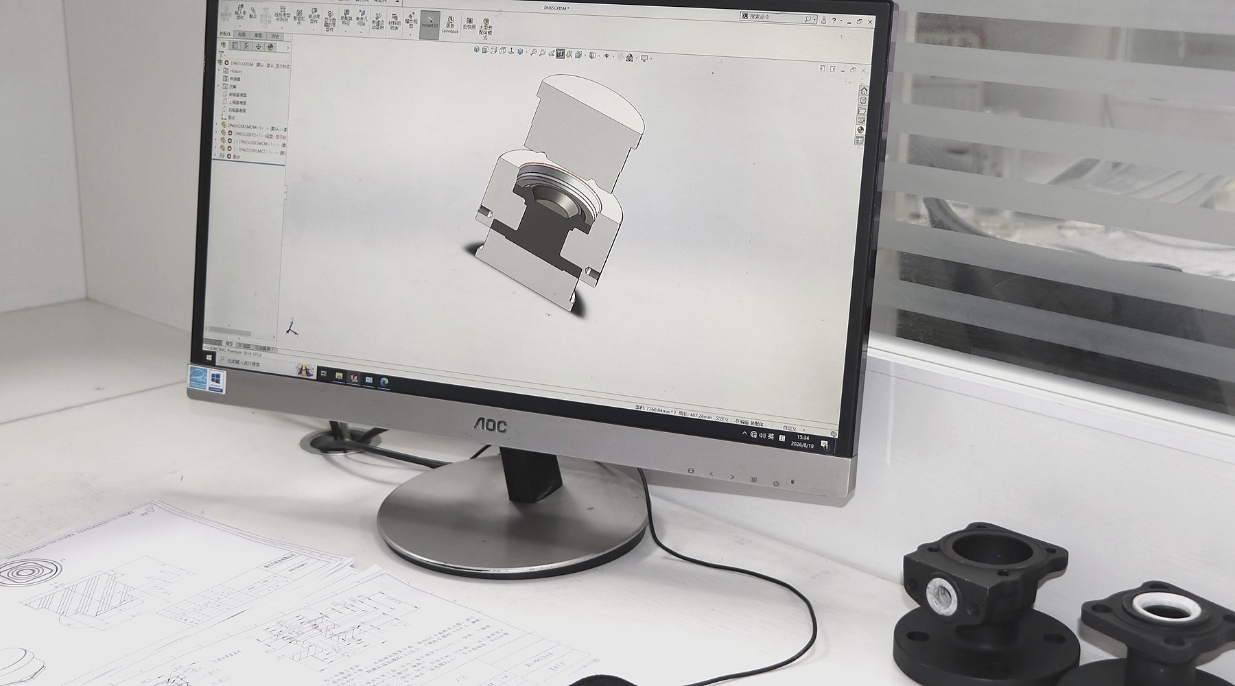 A ball valve body modelled in section on the CAD workstation, with forged samples on the desk.